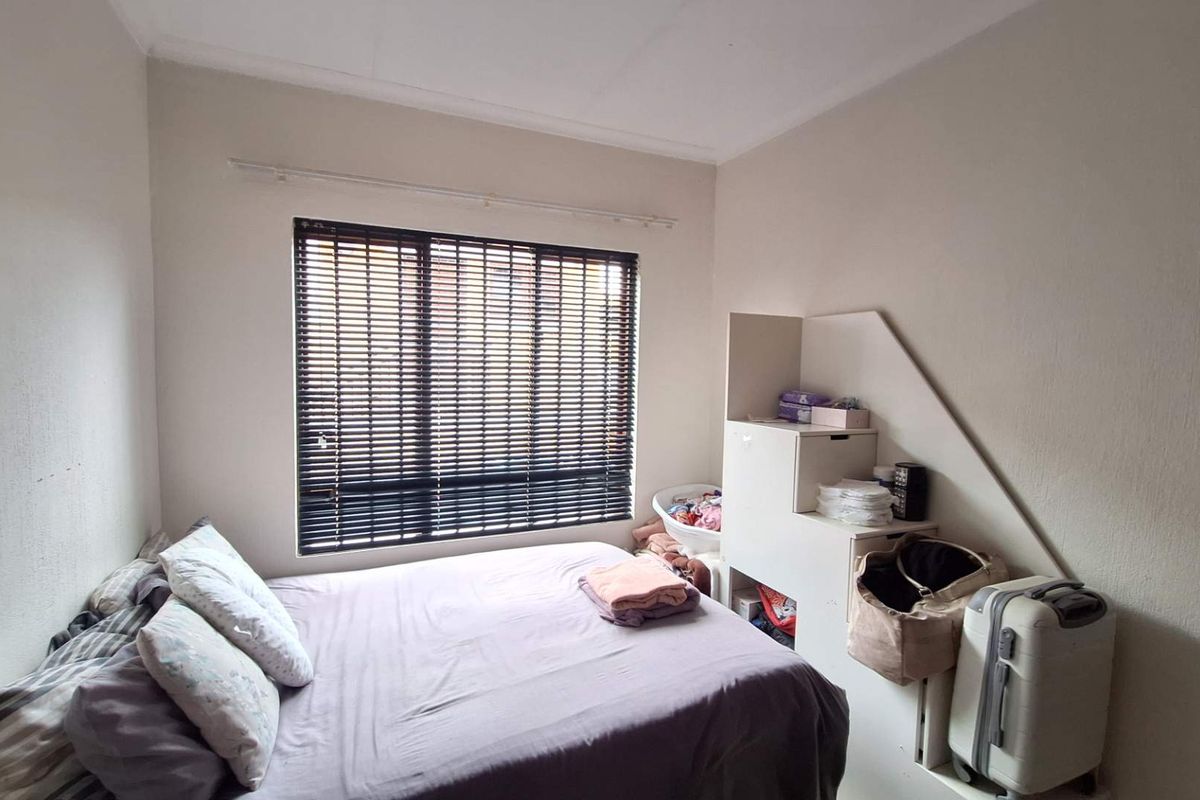 A standard bedroom featuring neutral walls and a window fitted with venetian blinds.