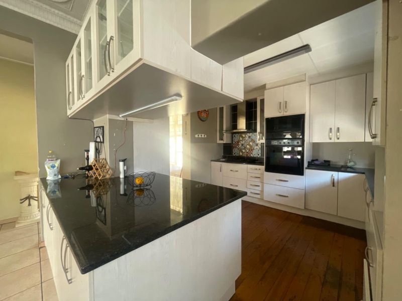 A functional kitchen featuring white cabinetry, dark granite countertops, built-in oven and microwave, and timber flooring with a breakfast bar island.