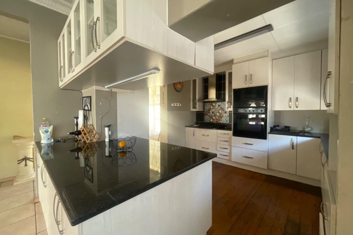 A functional kitchen featuring white cabinetry, dark granite countertops, built-in oven and microwave, and timber flooring with a breakfast bar island.