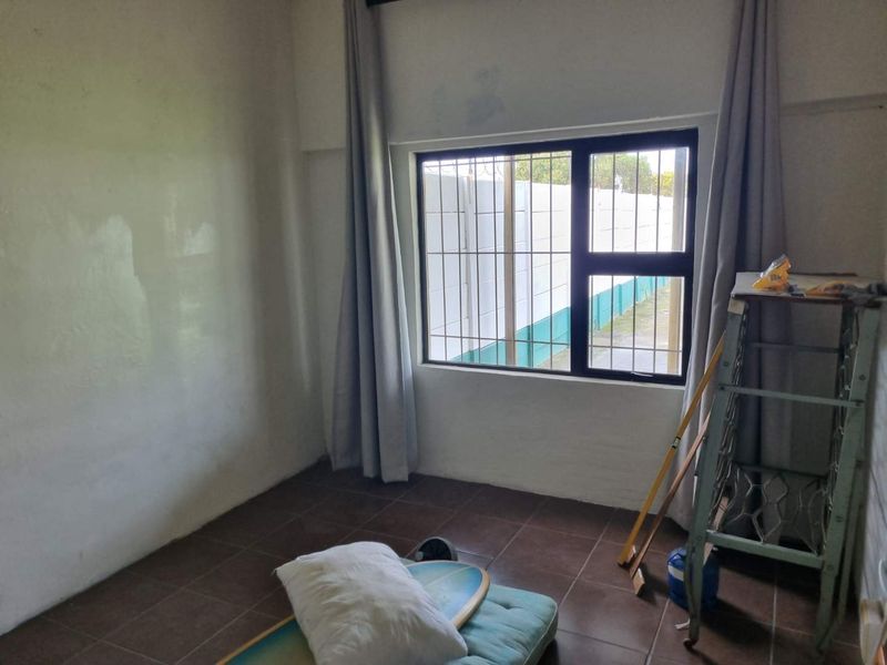 A simple bedroom featuring tiled flooring and a window fitted with security bars, offering a blank canvas for potential interior updates.