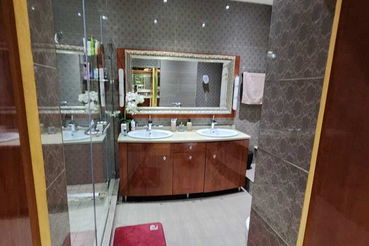 A well-maintained bathroom featuring a double vanity with integrated sinks, large wall-mounted mirror, tiled walls, and a glass shower enclosure.