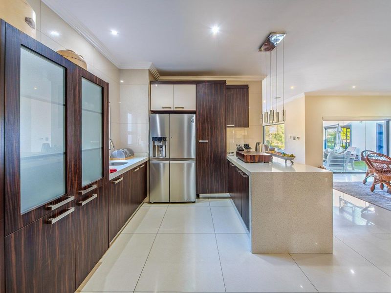 Modern kitchen featuring dark wood cabinetry, stone countertops, a central island, and high-quality tiled flooring, seamlessly flowing into the adjacent living area.