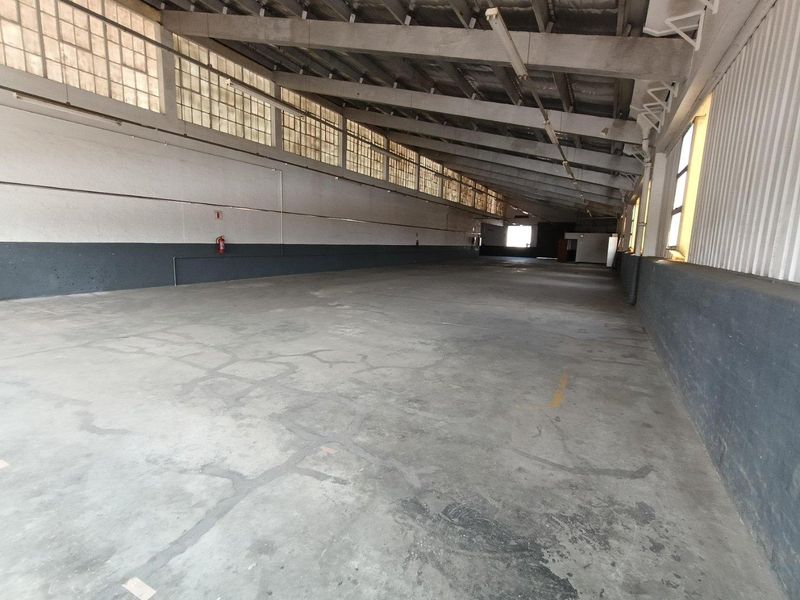 Spacious industrial warehouse unit featuring high ceilings with exposed steel trusses, clerestory windows for natural light, and durable concrete flooring.