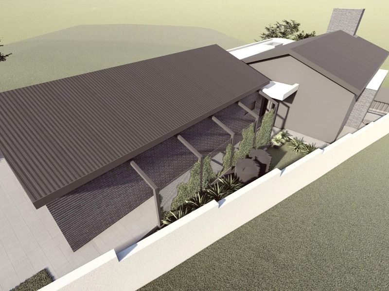 An aerial perspective of a modern residential property featuring a corrugated metal roof, brick exterior, and a secure perimeter wall.