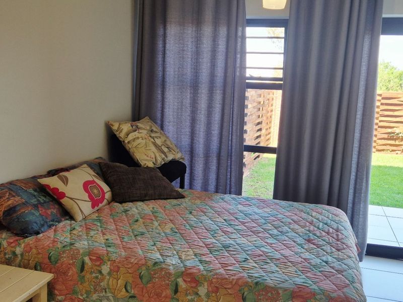 A bright bedroom featuring tiled flooring and a sliding glass door that provides direct access to an outdoor patio and garden area.