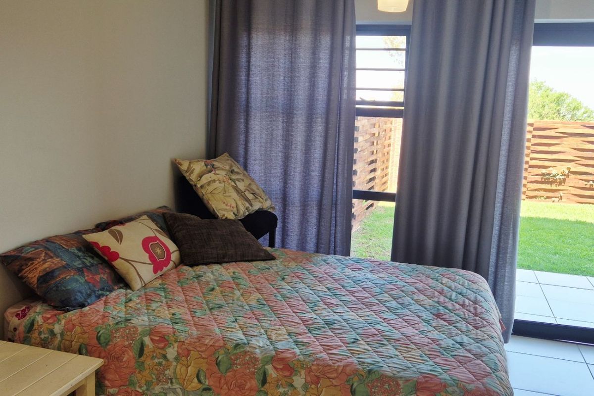 A bright bedroom featuring tiled flooring and a sliding glass door that provides direct access to an outdoor patio and garden area.