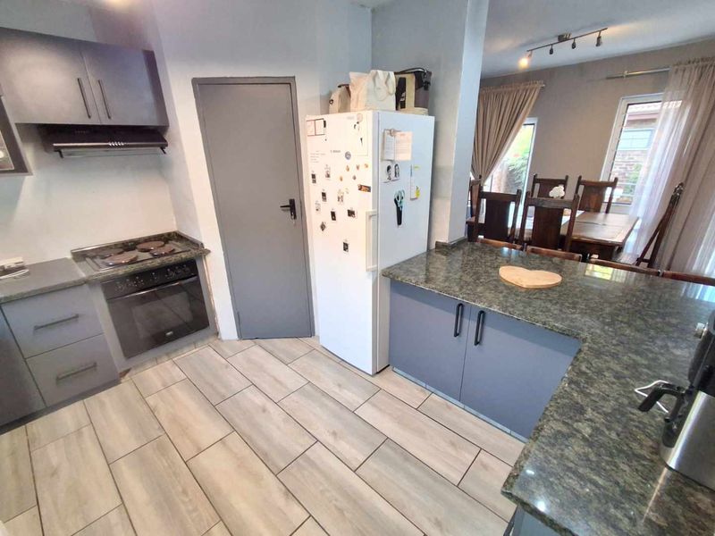 Open-plan kitchen featuring modern grey cabinetry, granite countertops, built-in oven and hob, flowing into a dining area with tiled flooring throughout.