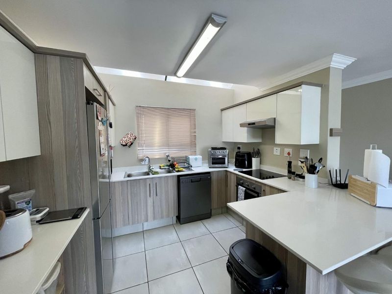 A functional kitchen featuring modern wood-grain and white cabinetry, stone countertops, integrated appliances, and tiled flooring with ample workspace.