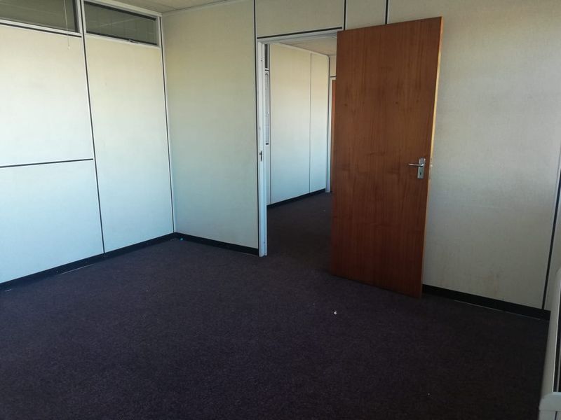 An empty office space featuring modular partition walls, dark carpeting, and a timber door, offering a blank canvas for professional workspace configuration.