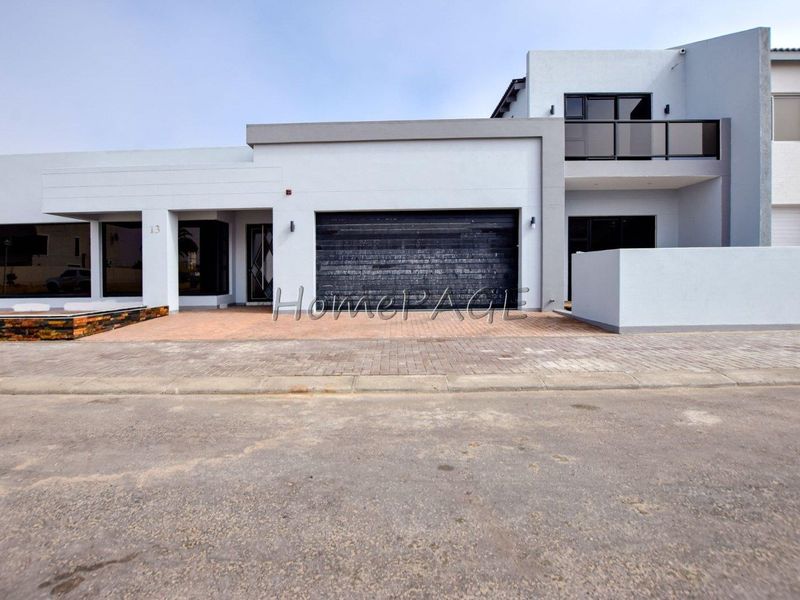 Modern double-story residential facade featuring a paved driveway, integrated double garage, and an upper-level balcony with glass balustrades.