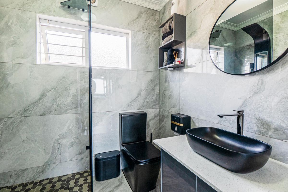 Modern bathroom featuring marble-look wall tiles, a walk-in shower with glass screen, black fixtures, and a sleek vanity with a vessel sink.