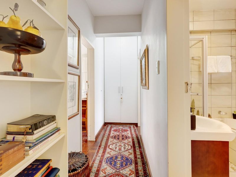 A bright hallway featuring parquet flooring, built-in storage cupboards, and integrated shelving, providing a clean transition between living areas and the bathroom.
