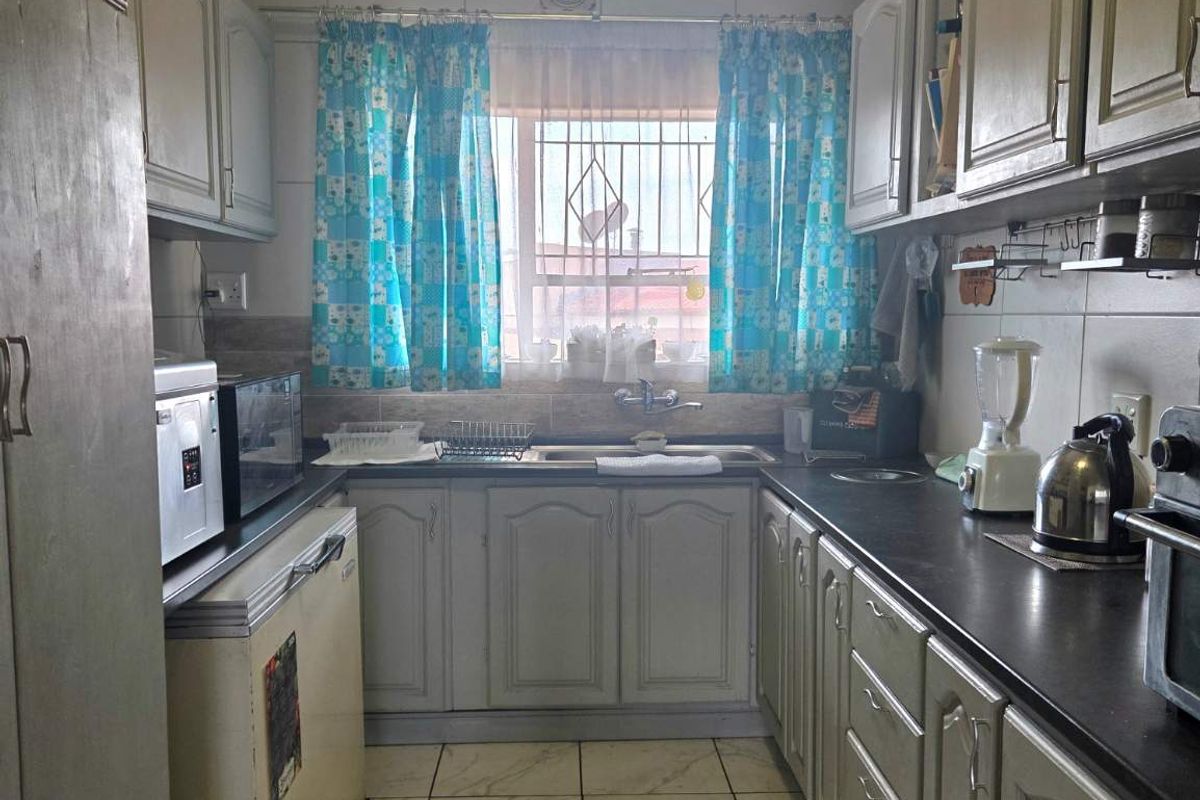 A functional galley-style kitchen featuring built-in cabinetry, dark countertops, a stainless steel sink, and tiled flooring with a window for natural light.