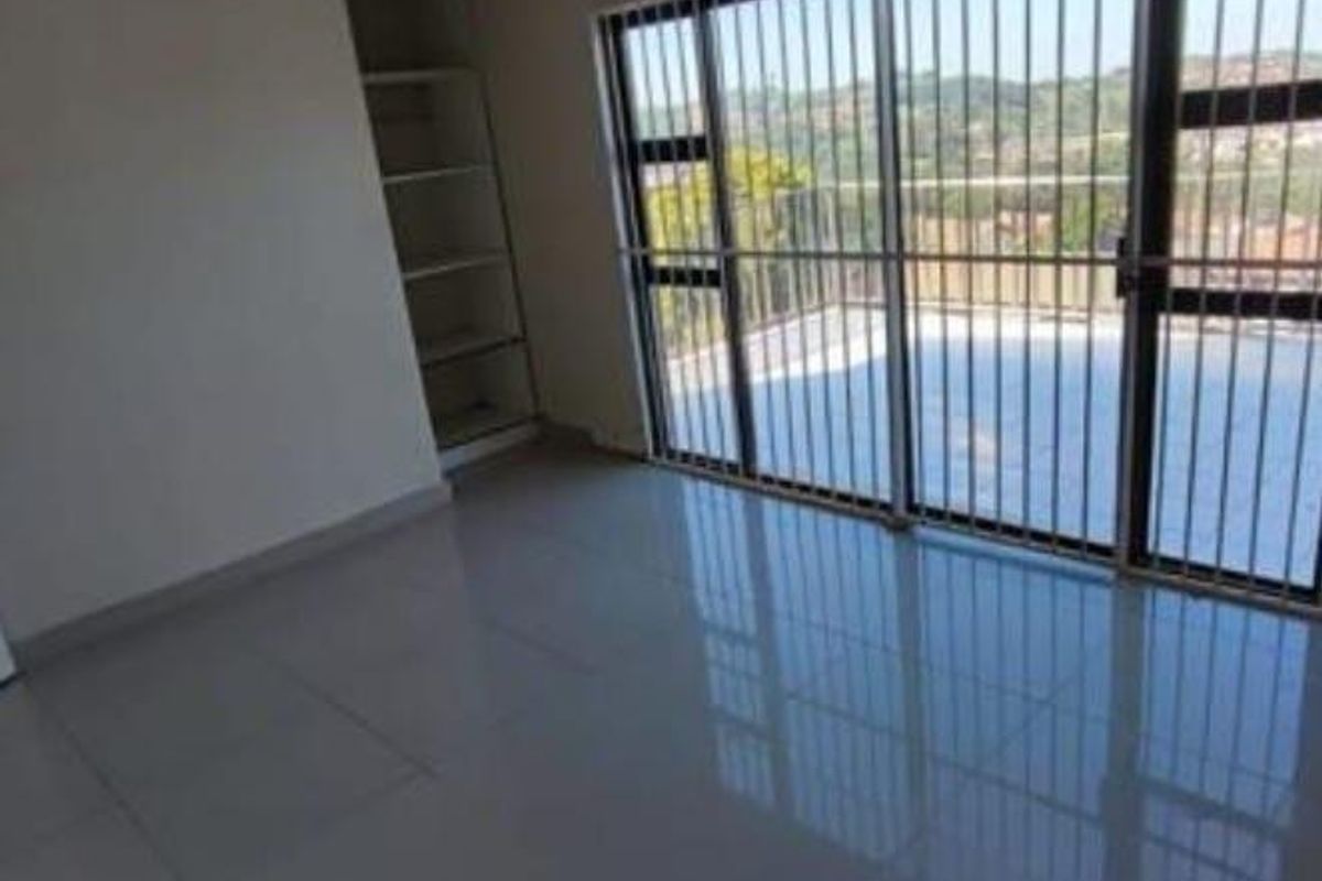 An empty bedroom featuring tiled flooring, built-in shelving, and a large sliding glass door with security bars leading to an outdoor area.