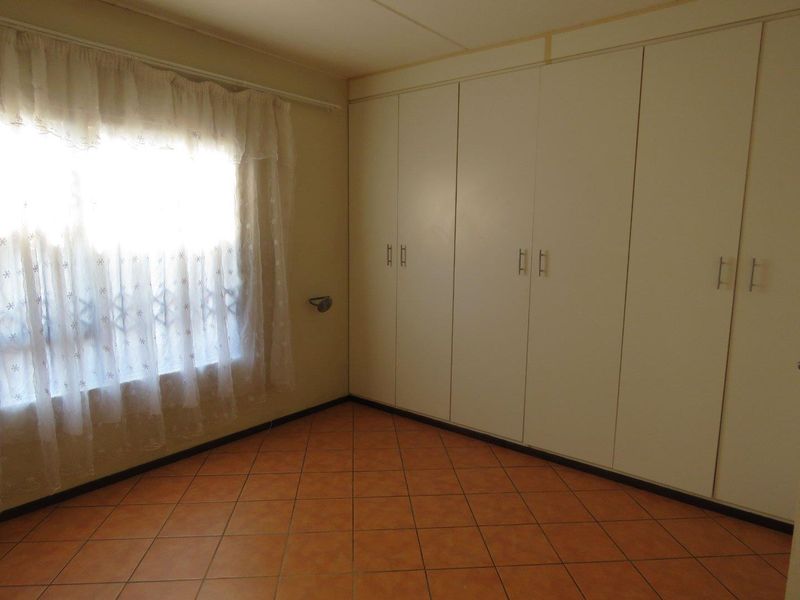 A vacant bedroom featuring tiled flooring and extensive built-in cupboard storage space.