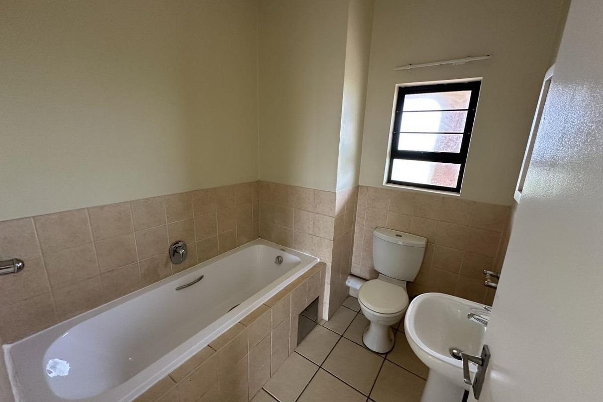 A functional bathroom featuring a bathtub, pedestal basin, and toilet with neutral tiled finishes and natural light from a window.
