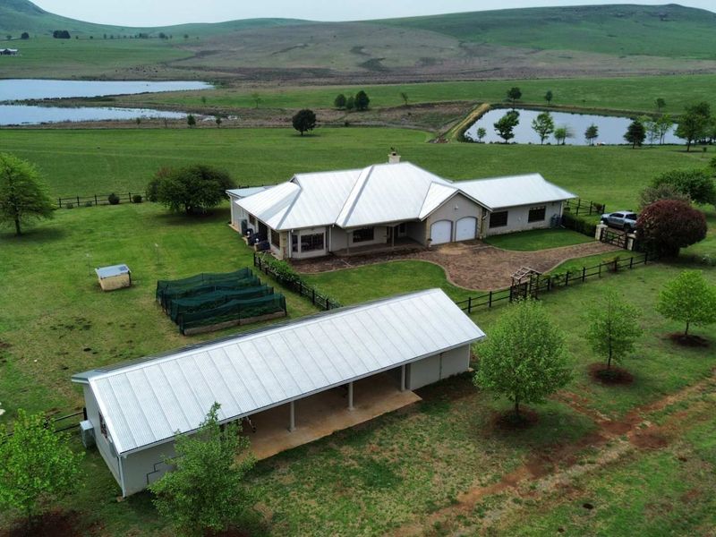 Aerial view of a farm property featuring a main residence with a metal roof, a double garage, and a separate outbuilding set in expansive grounds.