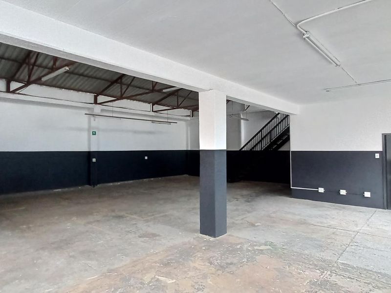 Spacious industrial utility area featuring exposed roof trusses, concrete flooring, and an internal staircase, suitable for workshop or storage use.