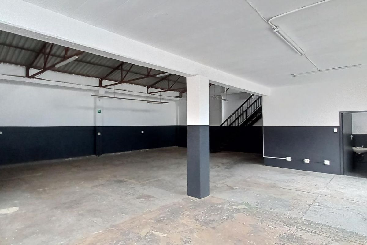 Spacious industrial utility area featuring exposed roof trusses, concrete flooring, and an internal staircase, suitable for workshop or storage use.