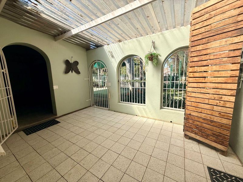 A covered patio area featuring tiled flooring, arched windows with security bars, and a timber privacy screen, offering a functional outdoor space.