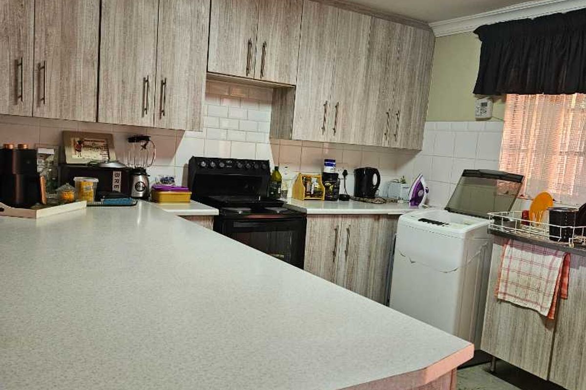 Kitchen featuring wood-look laminate cabinetry, a breakfast bar, tiled backsplash, and integrated laundry space with a top-loading washing machine.