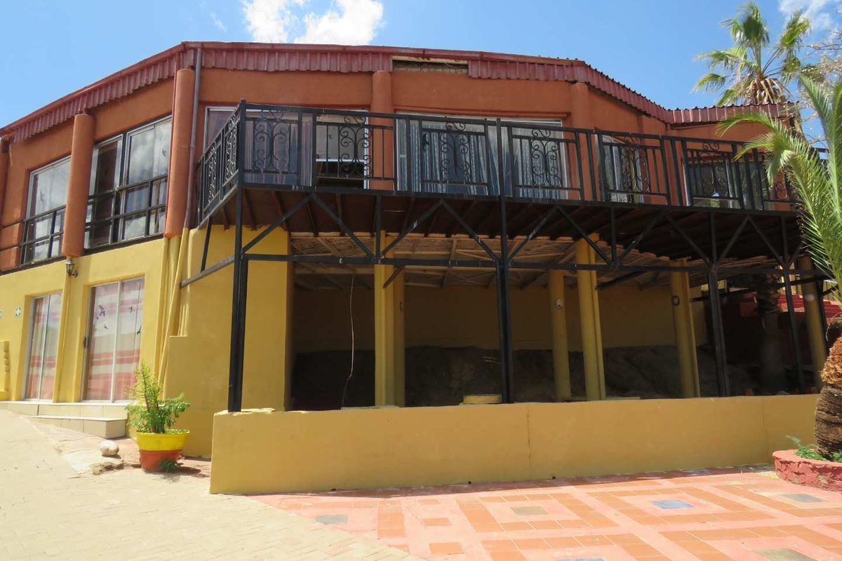 Rear elevation of the property featuring a raised deck with metal balustrades, paved patio area, and sliding door access to the main building.