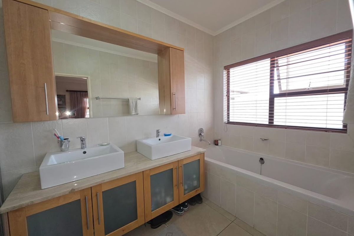 A well-maintained bathroom featuring a double vanity with vessel sinks, built-in cabinetry, and a bathtub with tiled surrounds.