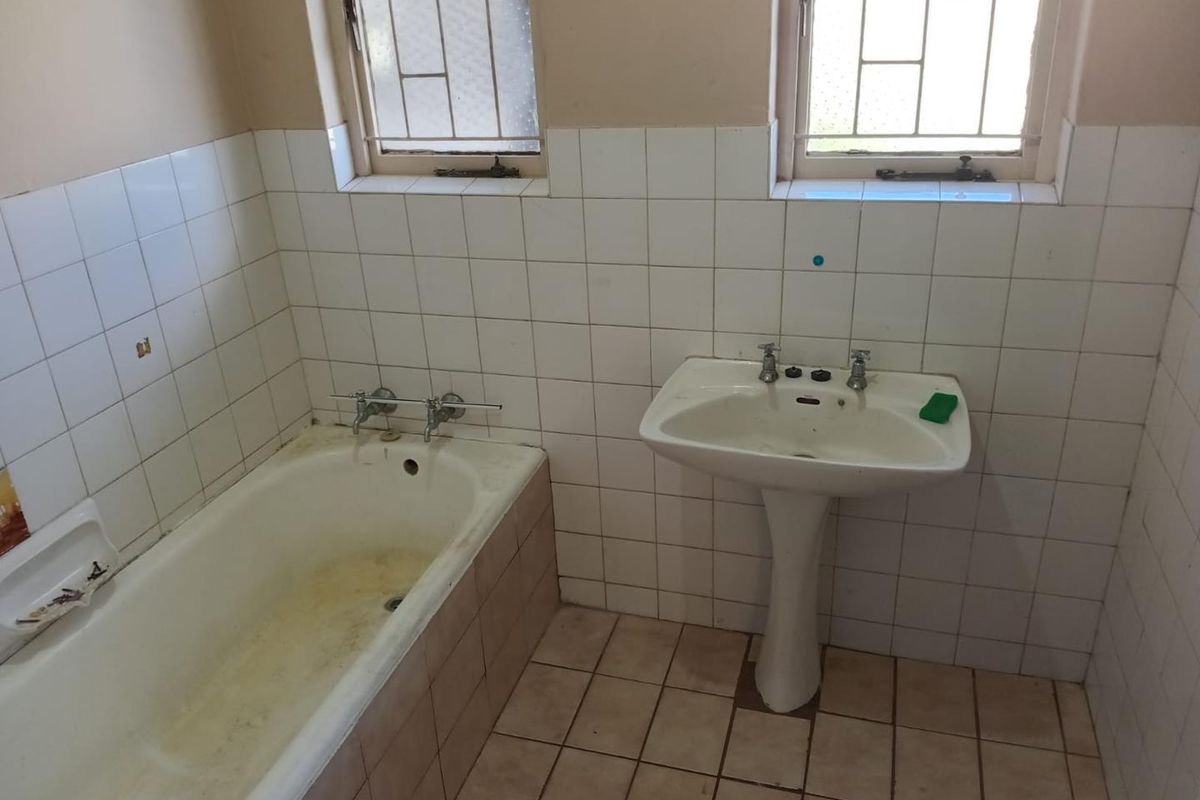A dated bathroom featuring a standard bathtub, pedestal basin, and tiled walls and flooring, requiring renovation to update the finishes and fixtures.
