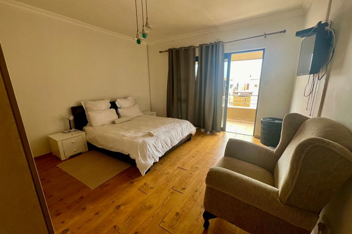 Spacious bedroom featuring warm timber flooring, direct access to a private balcony through sliding glass doors, and neutral wall finishes.