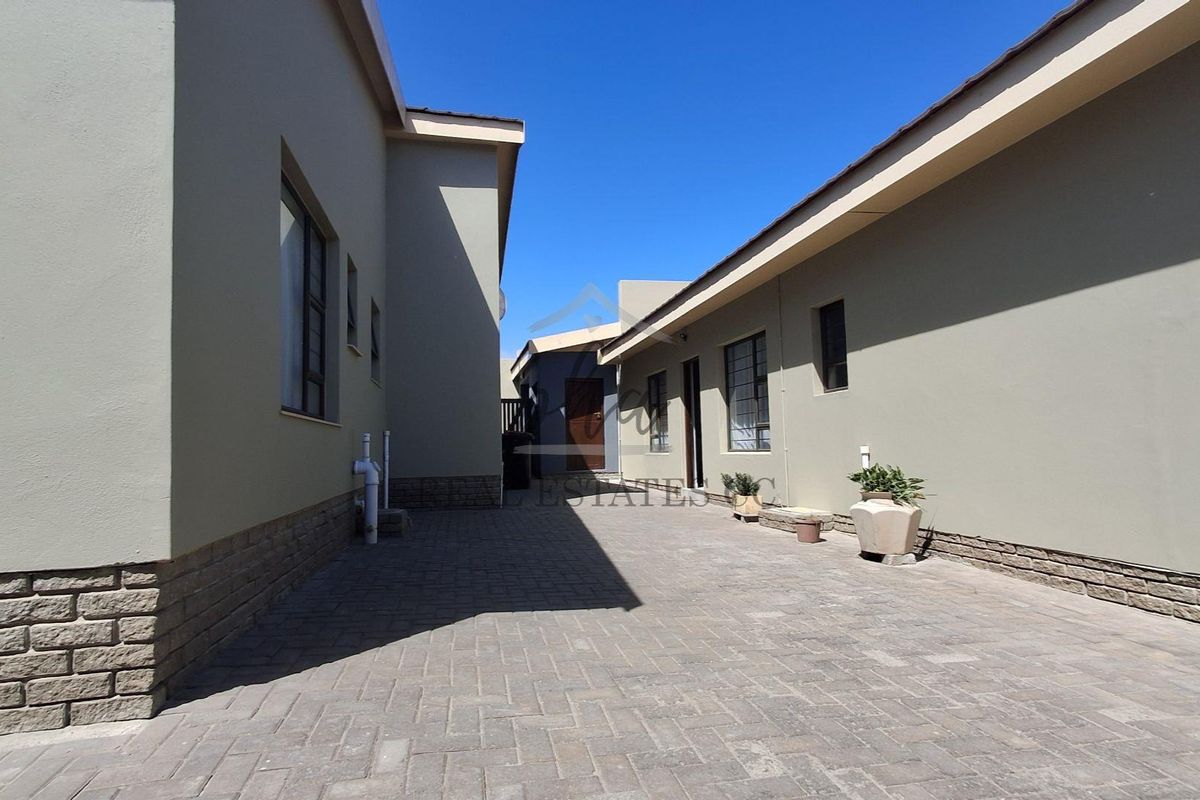 A paved rear courtyard area between two sections of the house, featuring stone cladding accents and modern aluminium window frames.