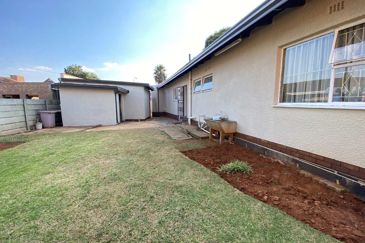 Rear exterior view of the house featuring a lawn, garden bed, and a detached outbuilding structure.