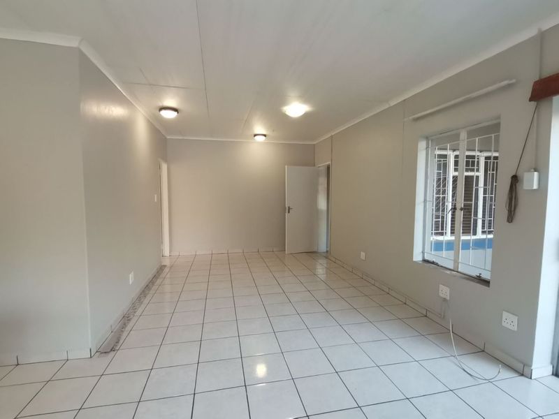 A bright, empty living area featuring neutral wall paint, tiled flooring, and security bars on the window.