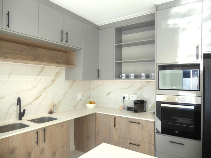 Modern kitchen featuring two-tone cabinetry, marble-look splashback, stone countertops, and integrated appliances including an oven and microwave.