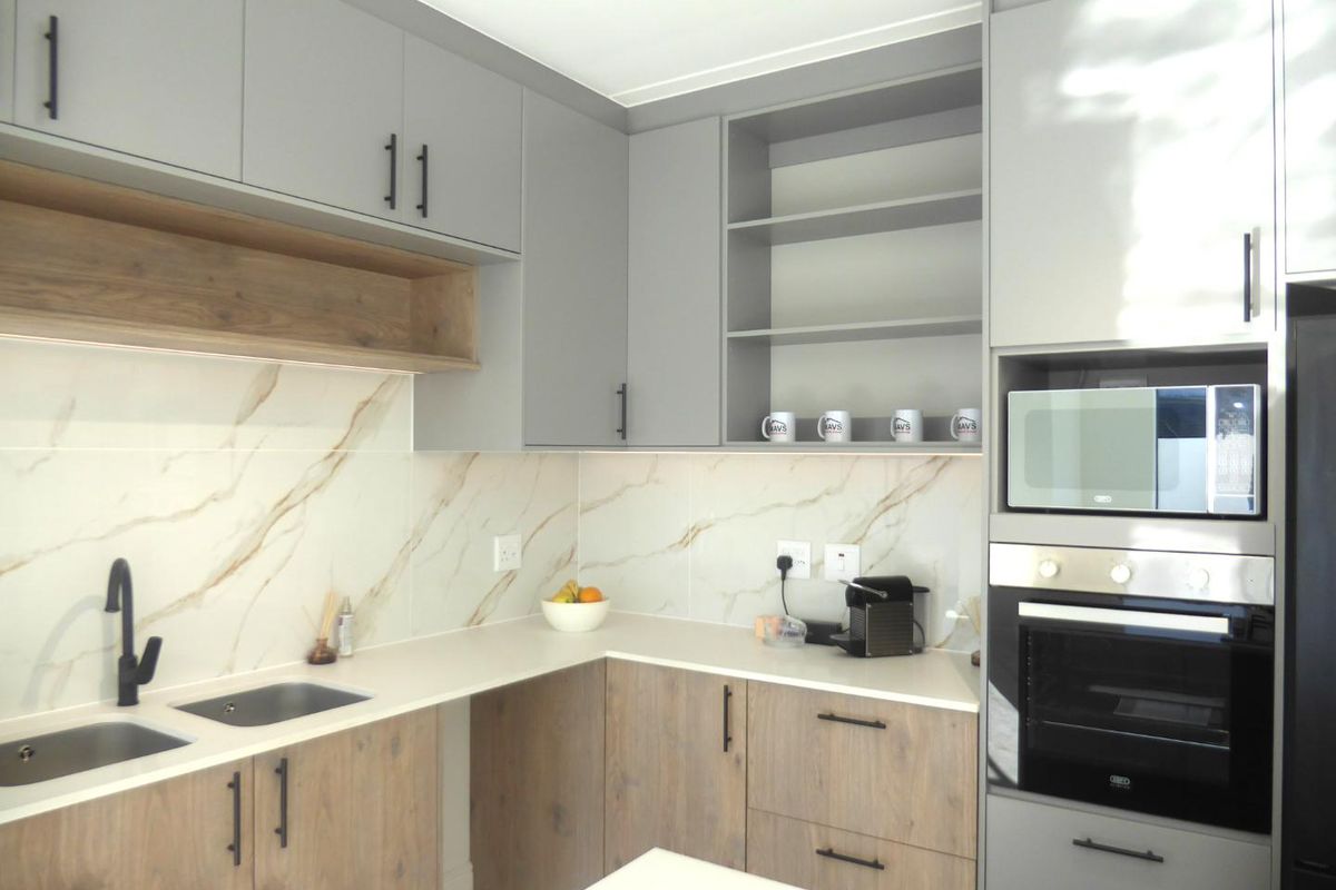 Modern kitchen featuring two-tone cabinetry, marble-look splashback, stone countertops, and integrated appliances including an oven and microwave.