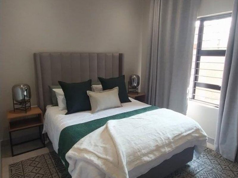 A well-maintained bedroom featuring neutral wall tones, tiled flooring, recessed downlighting, and a window fitted with security bars.