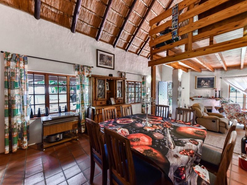 Open-plan living and dining area featuring a high thatched ceiling with exposed timber beams, a mezzanine level, and terracotta floor tiles.