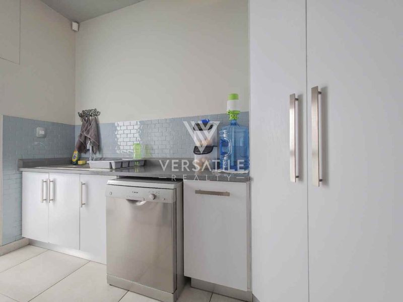A functional kitchen featuring white cabinetry, a tiled backsplash, stainless steel sink, and integrated dishwasher with neutral tiled flooring.
