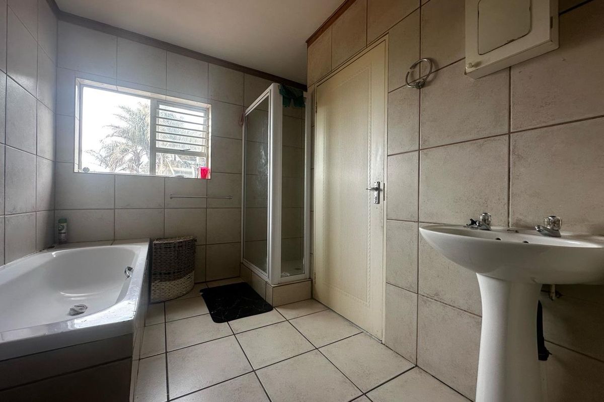 A functional bathroom featuring a pedestal basin, a built-in bathtub, and a separate shower enclosure with tiled walls and flooring.