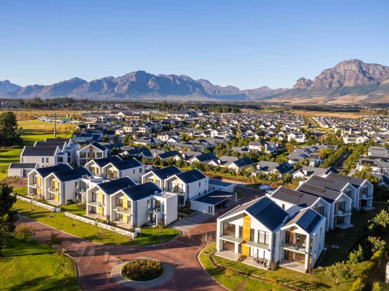 Aerial view of a modern residential estate featuring contemporary homes with solar panels, paved streets, and scenic mountain views in the background.