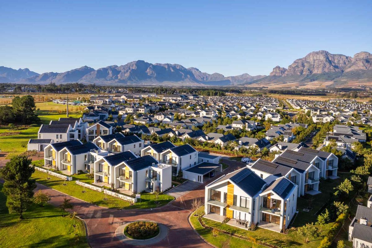Aerial view of a modern residential estate featuring contemporary homes with solar panels, paved streets, and scenic mountain views in the background.