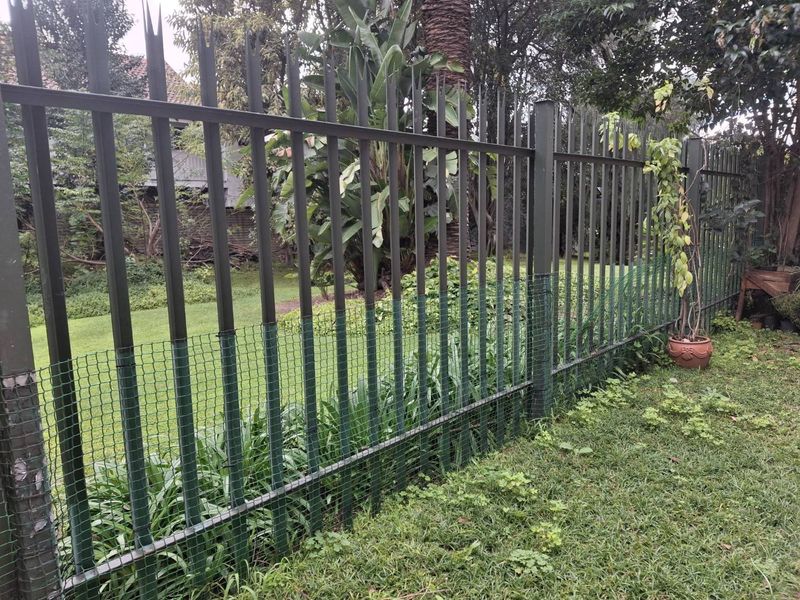 A view of the rear garden boundary featuring a metal palisade fence with additional green security mesh netting installed.