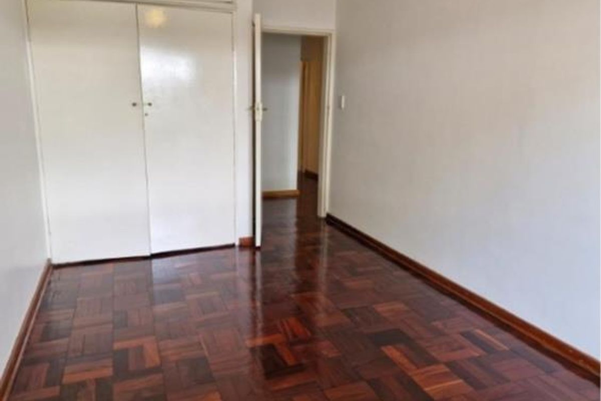 A vacant bedroom featuring polished parquet flooring and built-in storage cupboards, offering a clean and neutral space ready for personalization.