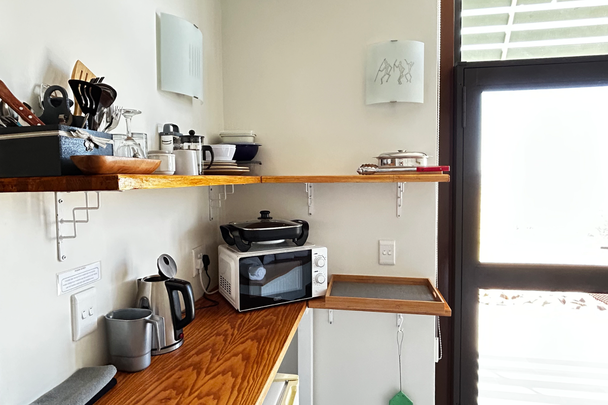 A functional kitchen corner featuring wooden countertops, open shelving, and a built-in microwave, providing efficient prep space with direct access to an exterior door.