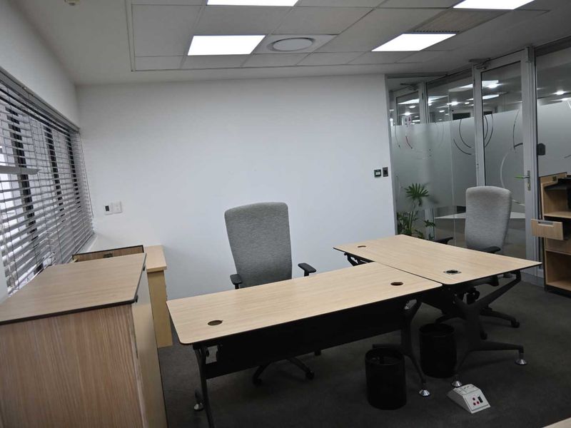 A professional office space featuring a suspended ceiling with recessed lighting, carpeted flooring, and a glass partition wall with privacy frosting.