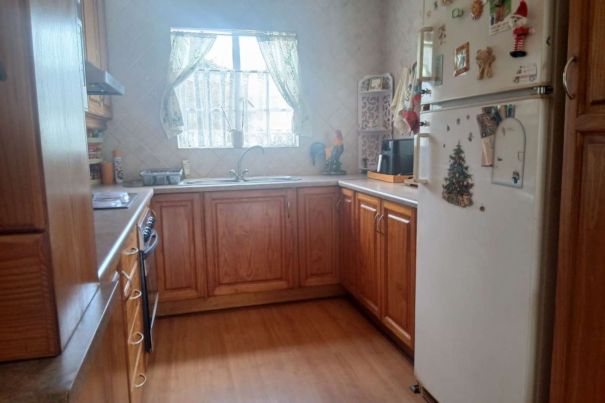A functional kitchen featuring traditional wooden cabinetry, laminate countertops, a stainless steel sink, and built-in cooking appliances with a tiled backsplash.