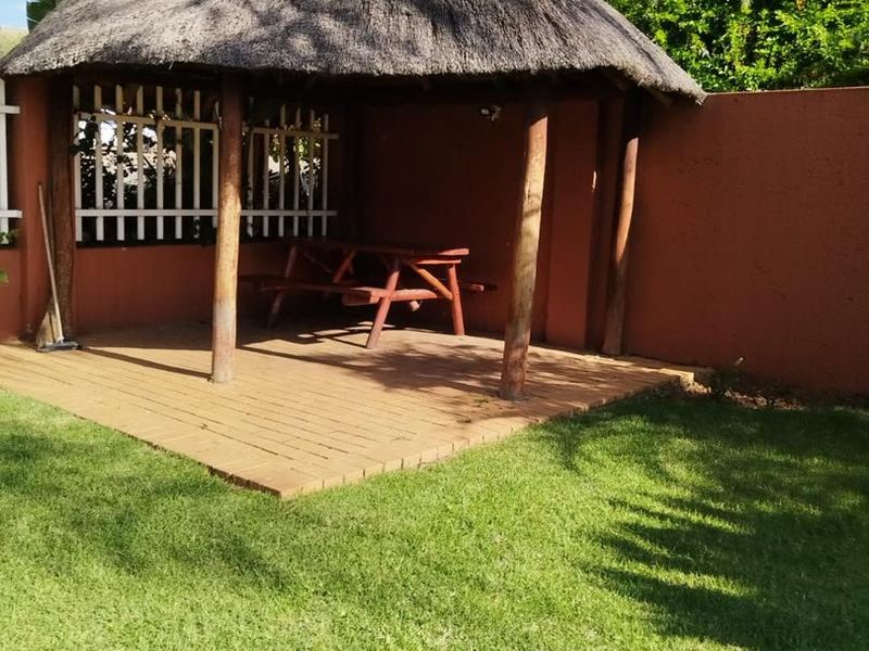 Outdoor thatched lapa area featuring a brick paved floor and wooden support posts, situated within a private garden setting.