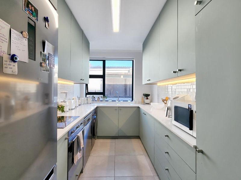 Modern galley-style kitchen featuring light green cabinetry, quartz countertops, under-cabinet lighting, and high-quality integrated appliances.