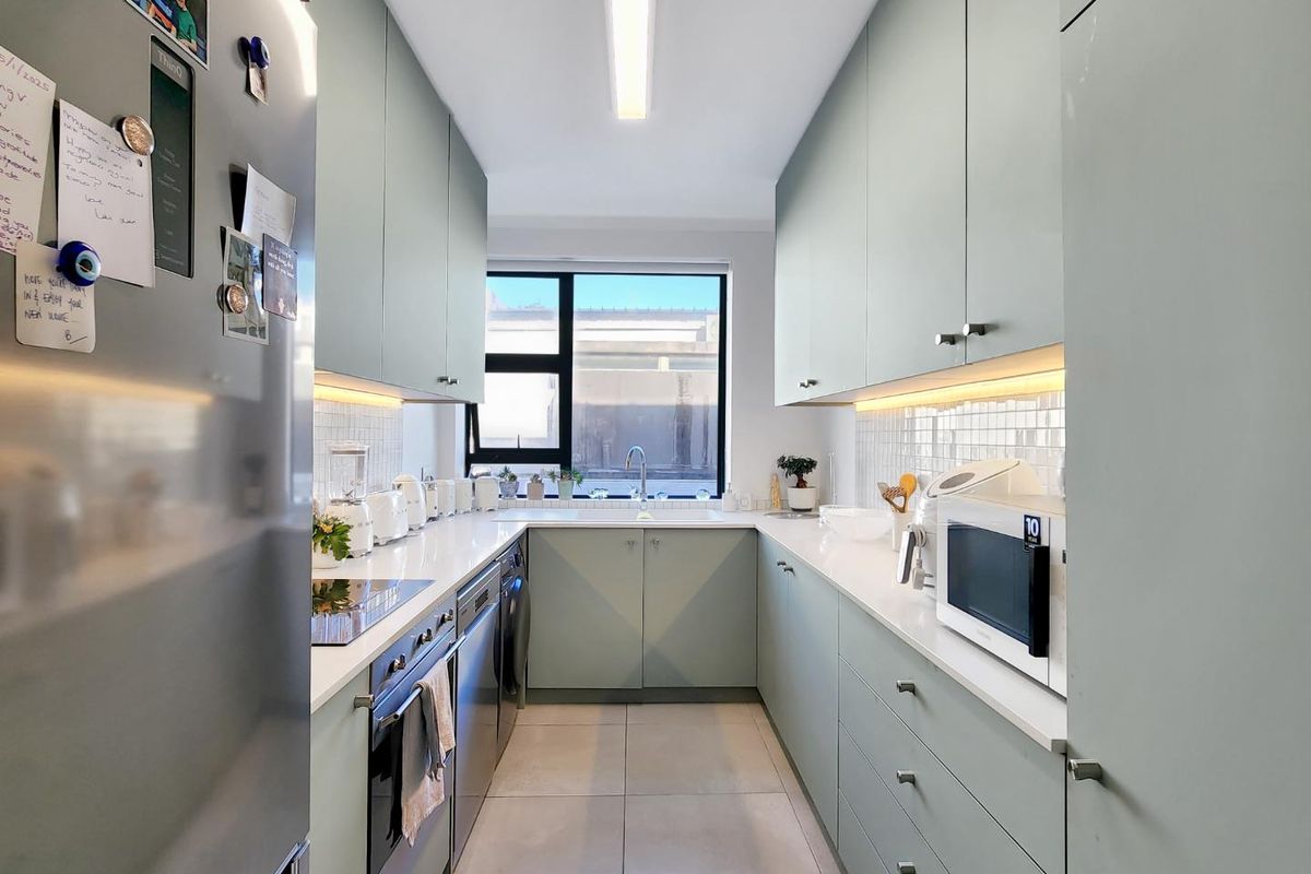 Modern galley-style kitchen featuring light green cabinetry, quartz countertops, under-cabinet lighting, and high-quality integrated appliances.