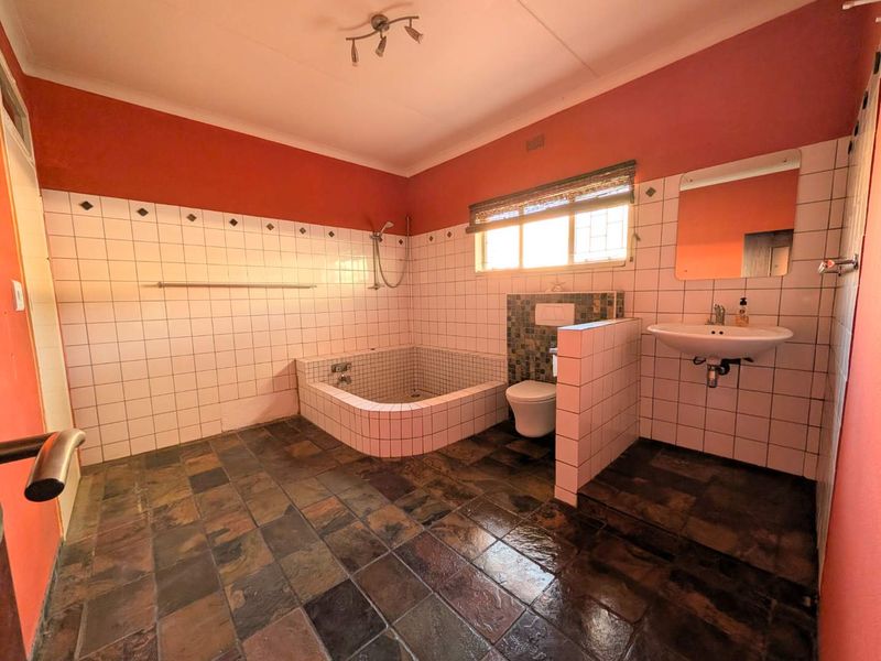 Spacious bathroom featuring a sunken tiled bathtub, wall-mounted toilet, and pedestal basin with slate-style floor tiles and contrasting wall finishes.