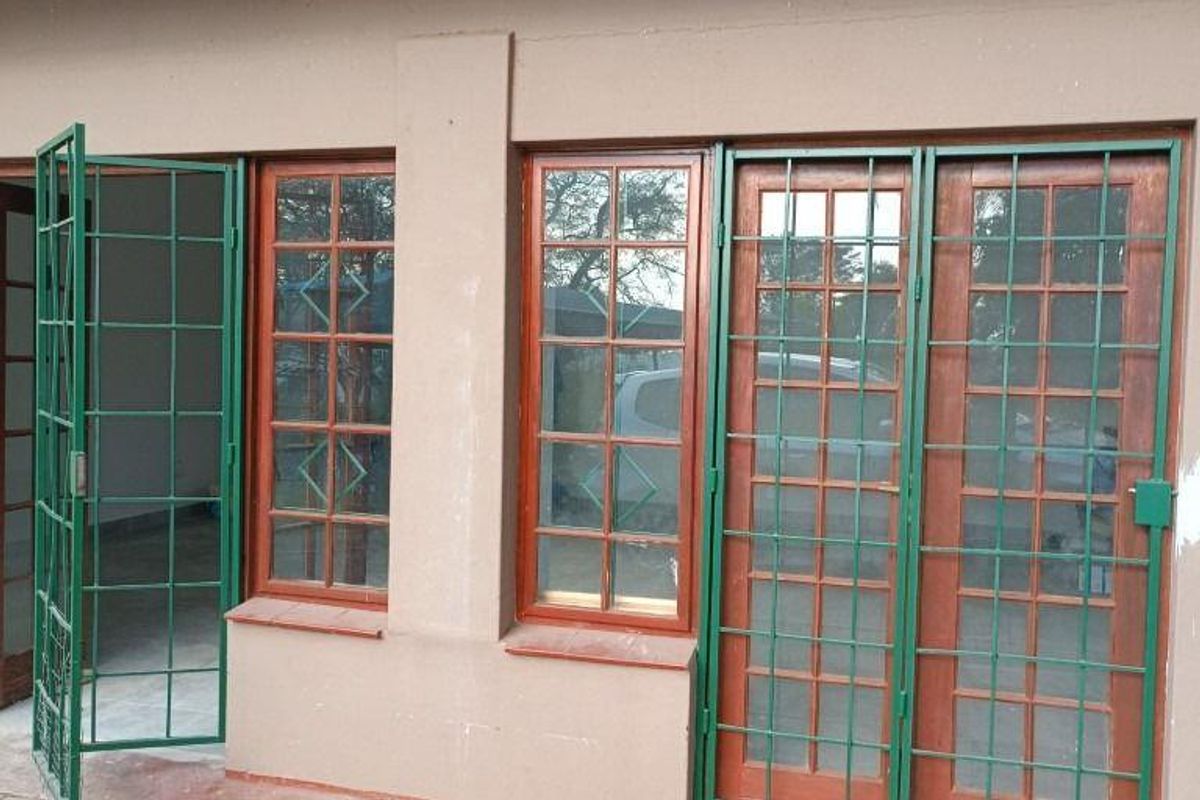 Rear exterior view featuring timber-framed doors and windows with green security gates, set against a paved patio area.